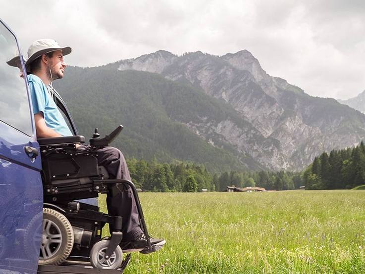 Mit dem Rollstuhl im Fahrzeug auf einer Wiese mit Ausblick auf die Berge